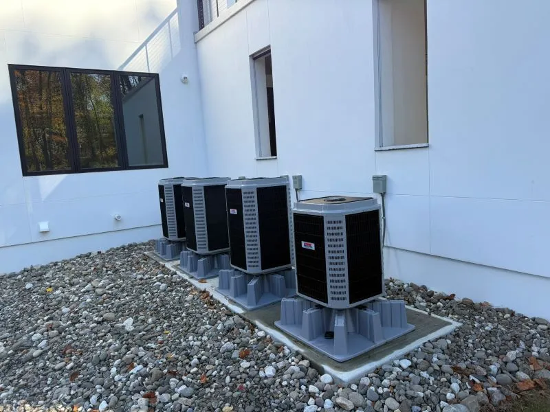 oltrom-ac6 Five outdoor air conditioning condensers on concrete pads along a white building, set on gravel.