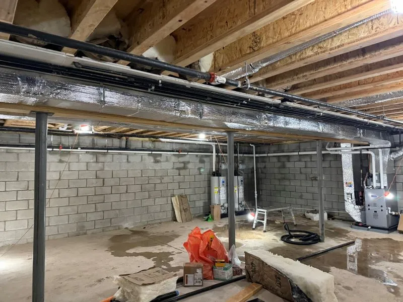 oltrom-ac7 Unfinished basement with exposed ceiling joists, ductwork, and concrete block walls; construction debris on the floor.